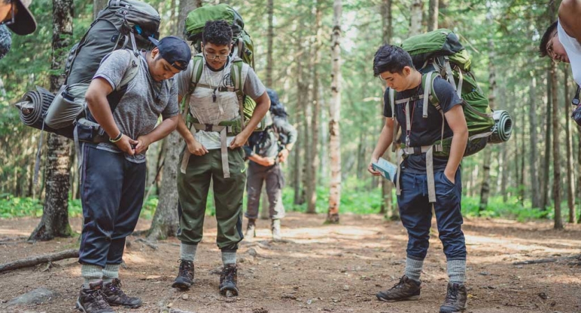 A group of students adjust their backpacks while standing in a wooded area.